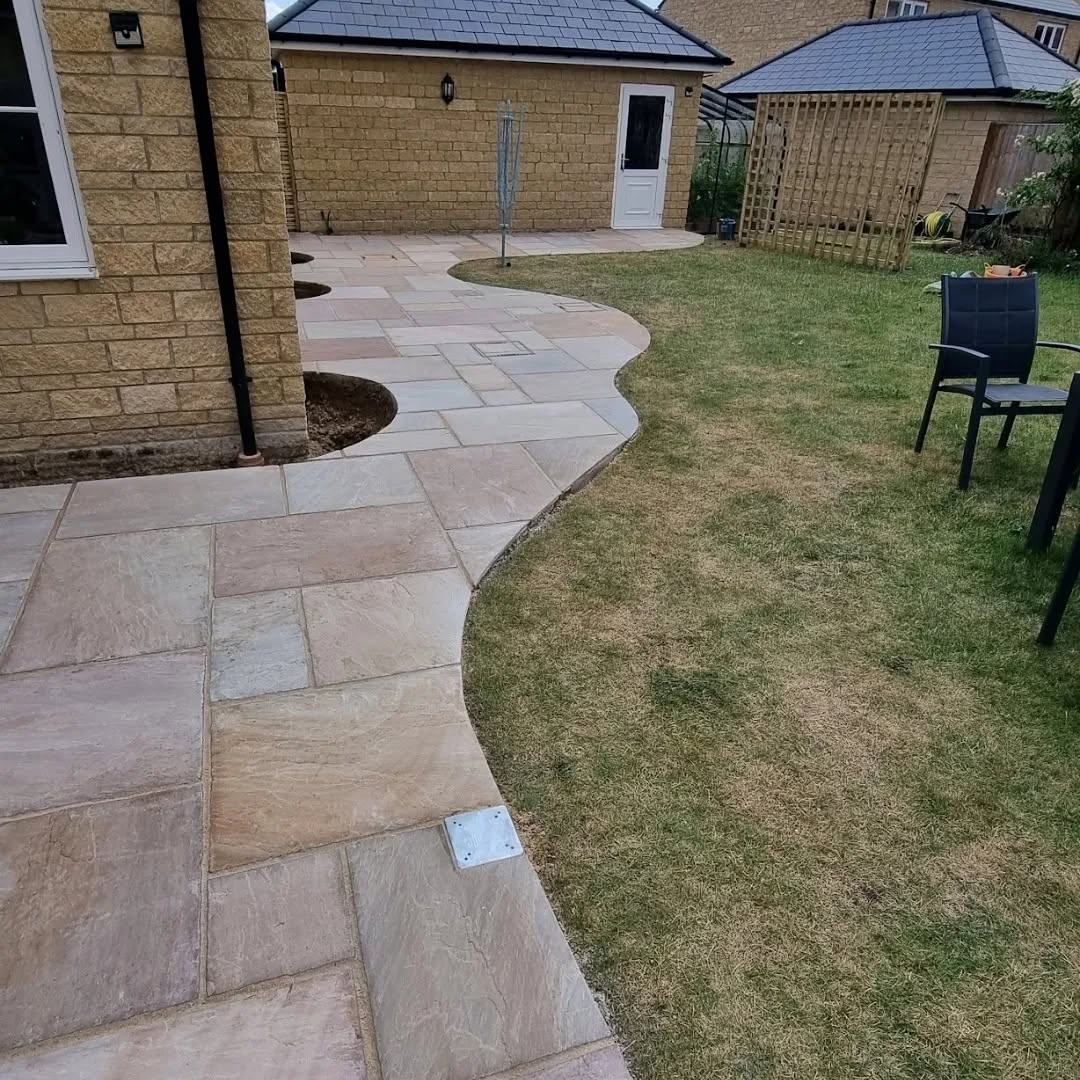 Curved sandstone path wrapping round a lawn beside a stone house