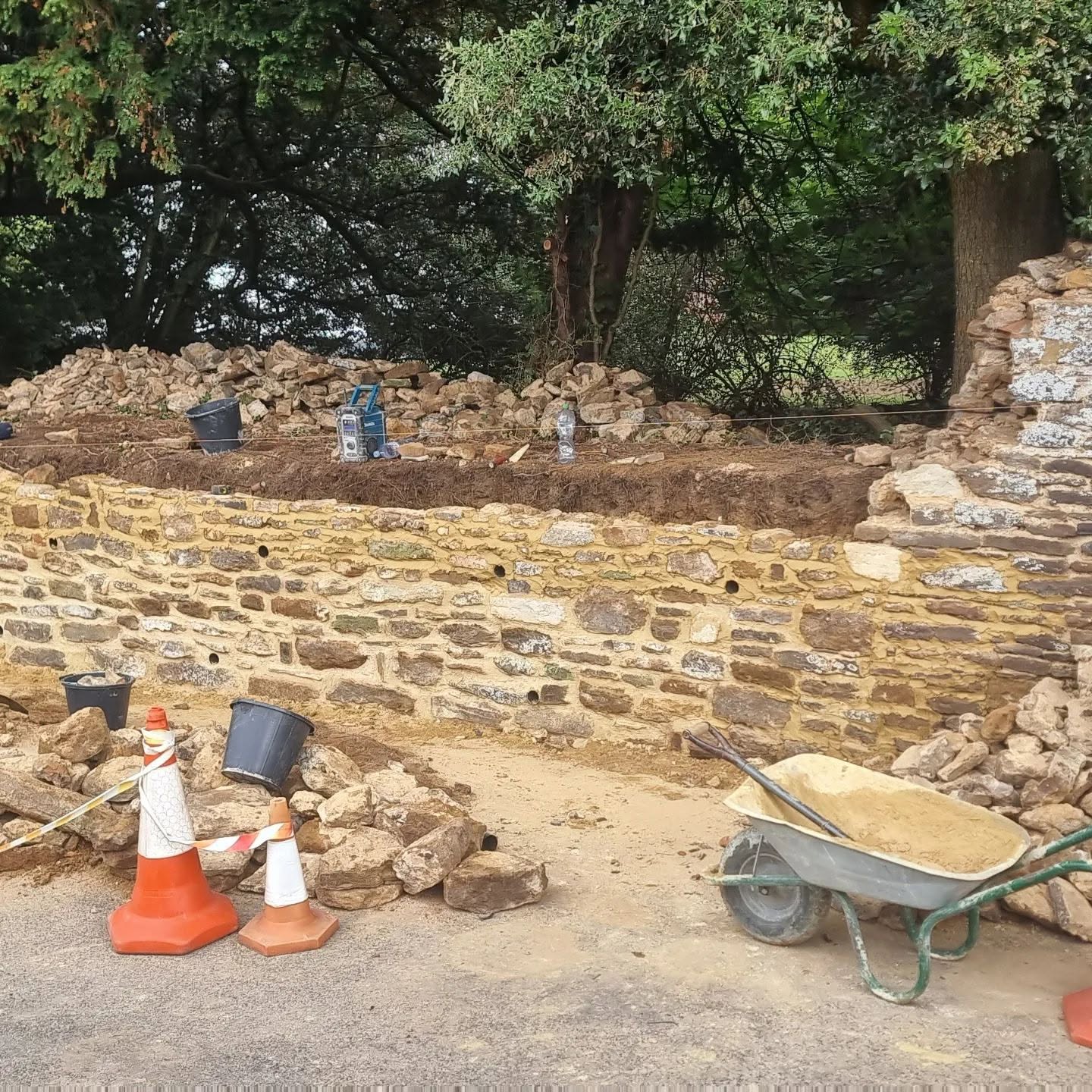 Roadside stone wall with cones, buckets and wheelbarrows on site