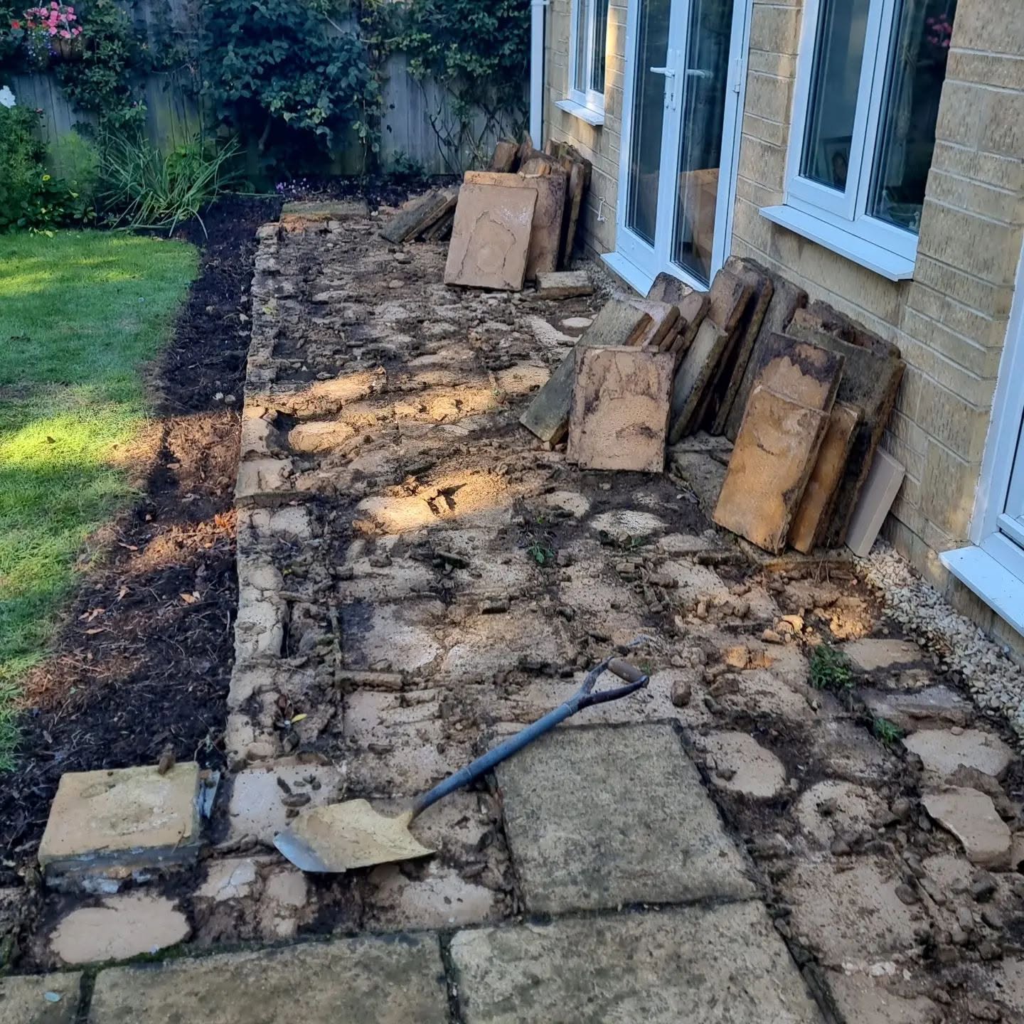 Old paving lifted beside a stone house, slabs stacked by the doors