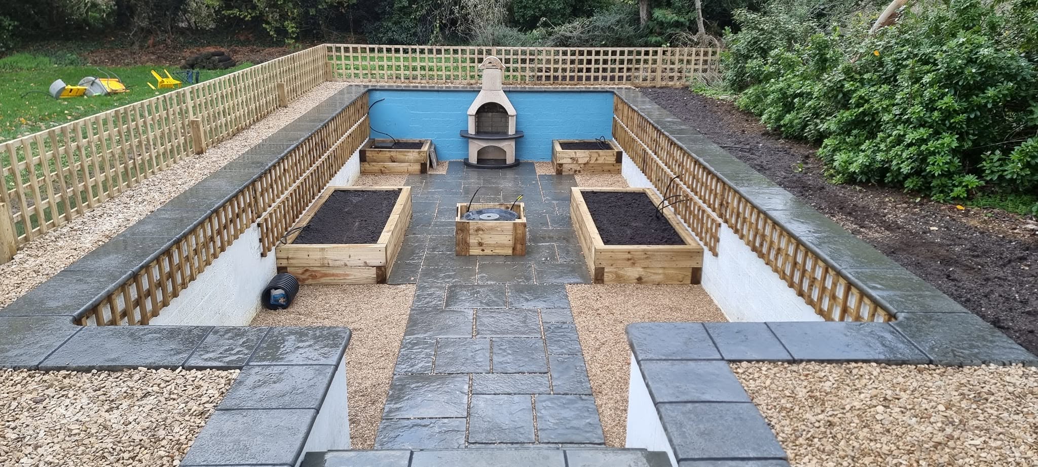 Sunken garden with slate paving, sleeper planters, gravel, trellis and a built-in pizza oven