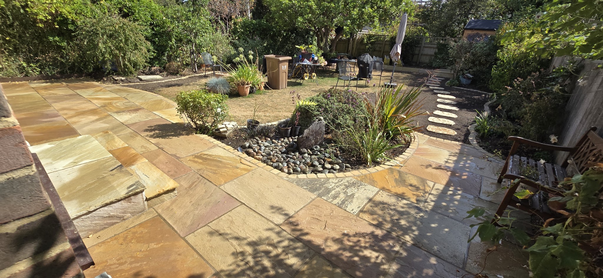 Curved Indian sandstone patio sweeping round a pebble and planting bed