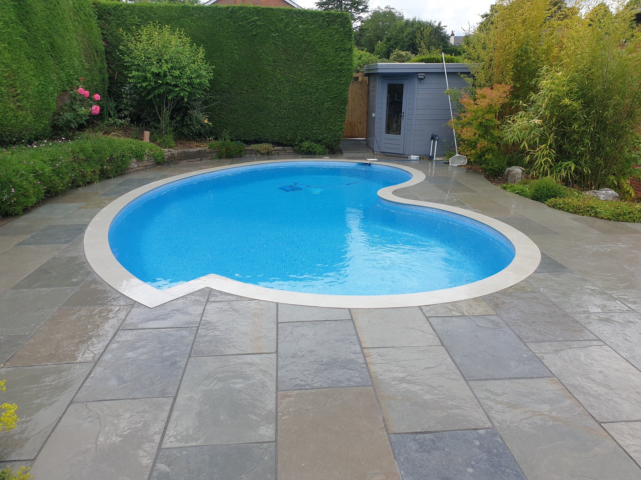 Grey stone paving laid around a kidney-shaped swimming pool