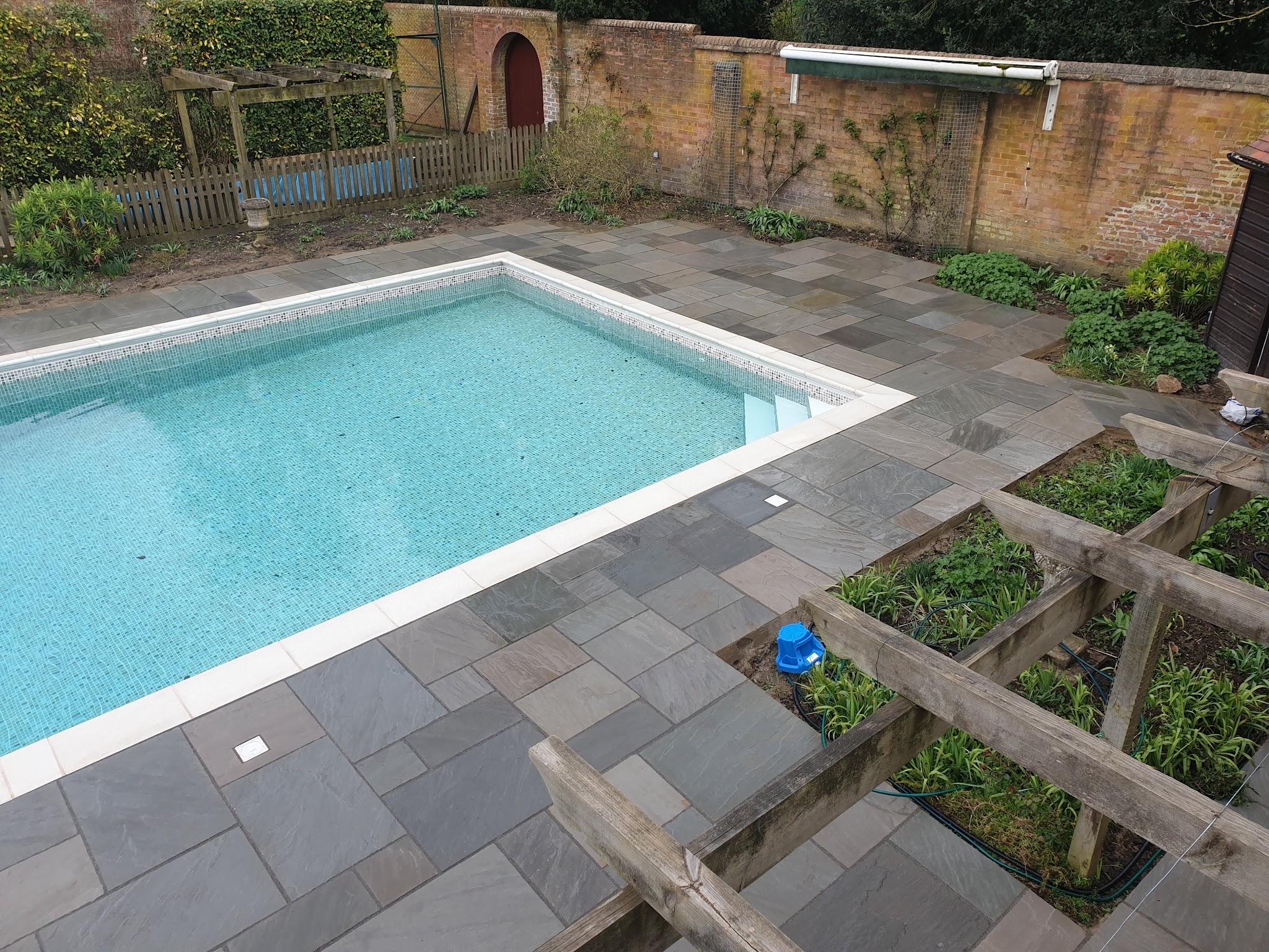 Grey paving around a rectangular pool in a walled garden