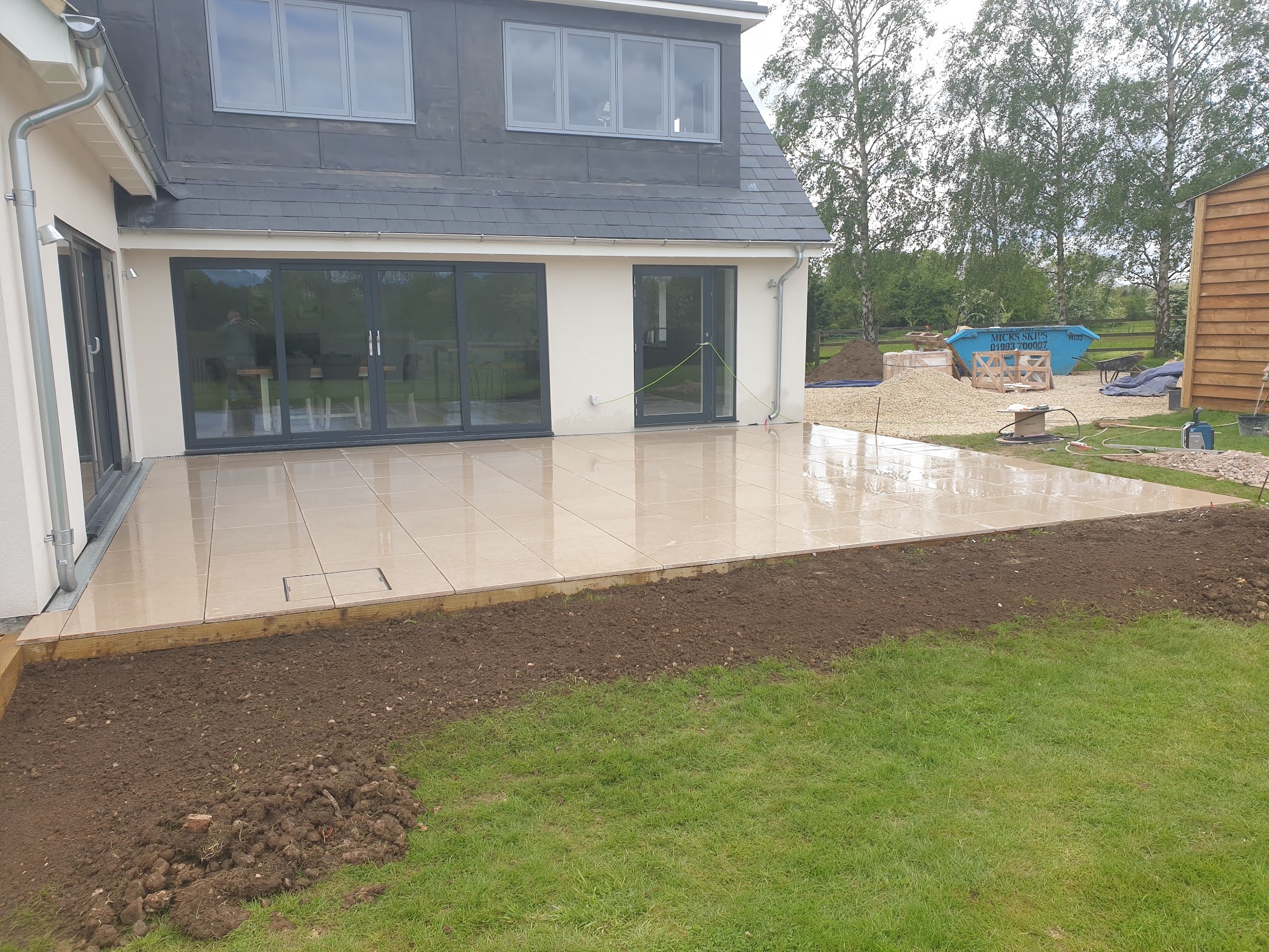 Large cream porcelain patio along the back of a modern house, with a new lawn edge
